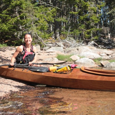 women crouching next to a moored kayak smiling at the camera