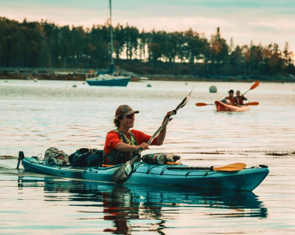 People kayaking on calm water with trees in the background.