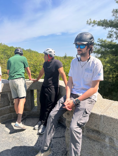 Three people with helmets standing and sitting on a stone structure, greenery in the background.